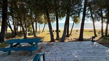 A wooden deck with a picnic table and benches overlooking a beach with trees and a clear view of the water.