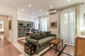 A modern living room with a sofa, a wooden coffee table, and a kitchen in the background. - Buccari Apartment - 3 Bedrooms with En-suite Bathrooms - Near the Vatican (Roma)