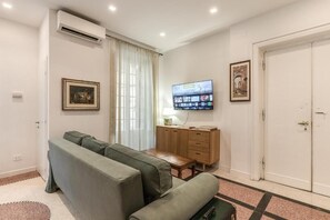 Een moderne woonkamer met een bank, een aan de muur bevestigde televisie, een houten kast en een deur.
