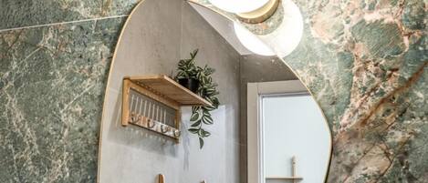 A bathroom with a marble wall, a wooden shelf with plants, a ladder, and a mirror.