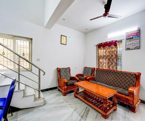 A living room with a sofa set, a coffee table, and a staircase with a railing. - Classic Leo's Home Stay (Katpadi)