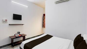 A hotel room with a bed, a flat-screen TV, an air conditioner, a bedside table with a coffee maker, and a power outlet.