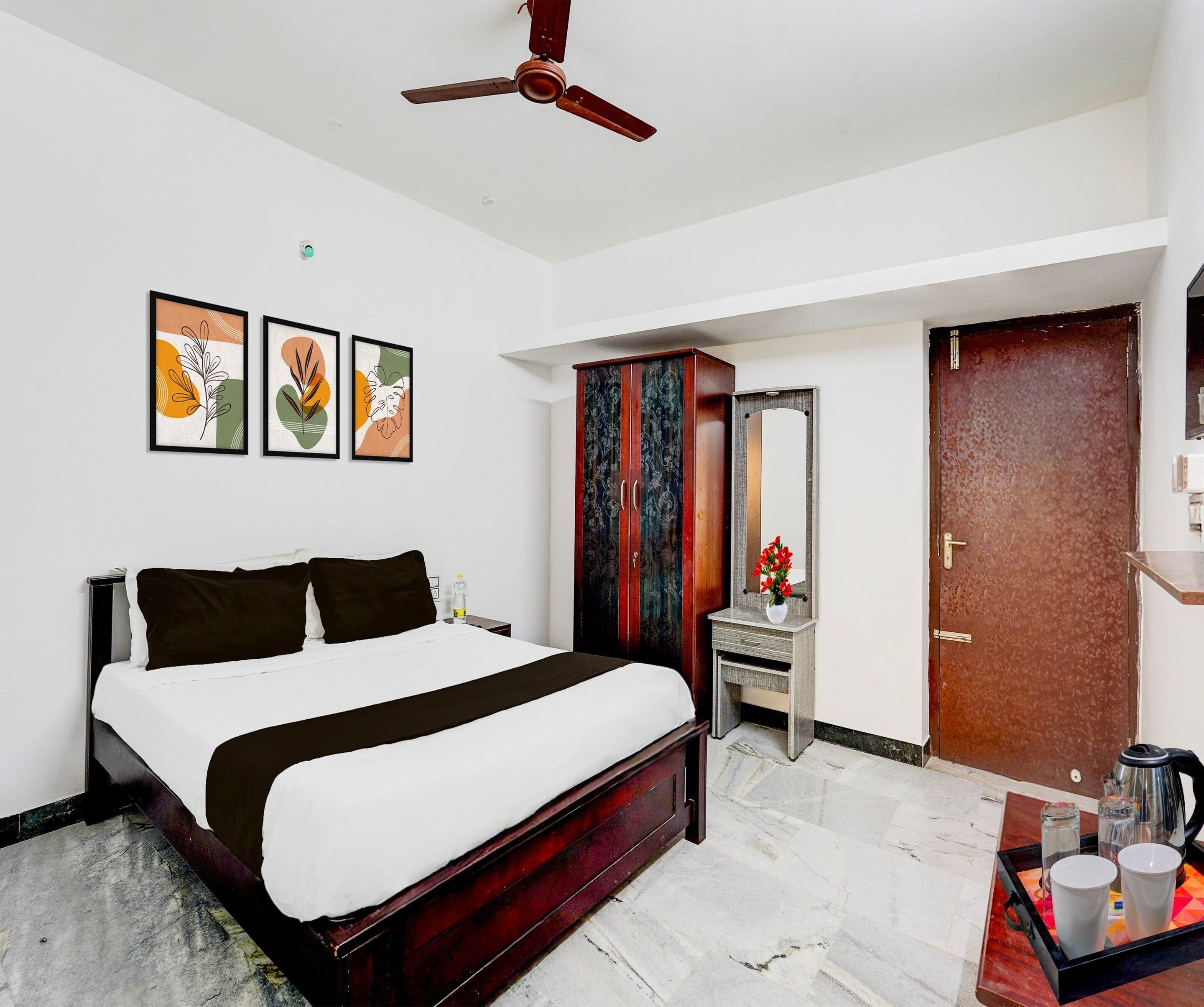 A hotel room with a bed, a desk, a wardrobe, a mirror, and a ceiling fan.