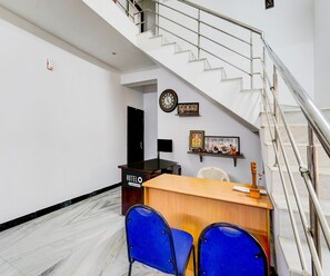 A hotel reception desk with a clock, a small shrine, and a staircase. - Classic Leo's Home Stay (Katpadi)