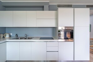 A modern kitchen with white cabinets, a stainless steel sink, and a built-in oven. - VerdeBlù - Home Design by the Sea (Arma di Taggia)