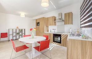 A modern kitchen with wooden cabinets, a built-in oven, and a dining area with a round table and red chairs. - Sliema-Gzira Stylish Apartment (Il-Gżira)