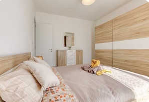 Een slaapkamer met een bed, een dressoir, een spiegel en een houten wandpaneel.