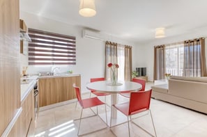 A modern kitchen with a built-in stove, a dining area with a round table and red chairs, and a living area with a sofa and a TV. - Sliema-Gzira Stylish Apartment (Il-Gżira)