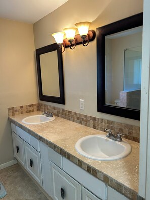 A bathroom with two sinks, a large mirror, and wall-mounted lighting. - Waterfront 1-bedroom apartment with AC in Palm Coast. Minutes to the beach. (Palm Coast)