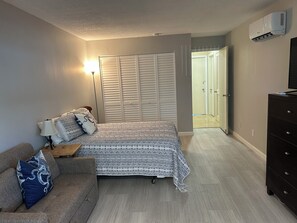 A bedroom with a bed, a nightstand, a dresser, a closet, and an air conditioning unit. - Waterfront 1-bedroom apartment with AC in Palm Coast. Minutes to the beach. (Palm Coast)
