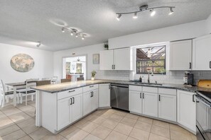 A modern kitchen with white cabinetry, a granite countertop, and a built-in dishwasher. - Private Pool + Bar - Pet Friendly - Sleeps 6 (Port Orange)