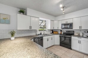 Een moderne keuken met witte kasten, granieten aanrechtbladen, roestvrijstalen apparatuur en een raam met uitzicht op een tuin.