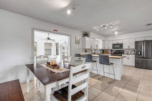 A modern kitchen with white cabinets, stainless steel appliances, and a dining area with a wooden table and white chairs. - Private Pool + Bar - Pet Friendly - Sleeps 6 (Port Orange)