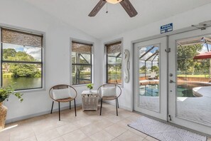 A sunlit room with a view of a lake, two wicker chairs, a small table, and a poolside door. - Private Pool + Bar - Pet Friendly - Sleeps 6 (Port Orange)