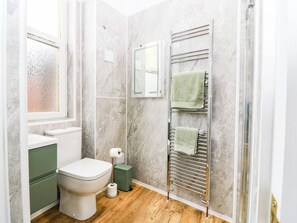 A bathroom with a toilet, a green trash bin, a towel rack with two towels, a mirror, and a window with frosted glass. - The Studio @ 18 (Kinross)