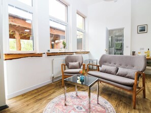 A modern living room with a sofa, armchair, and coffee table, large windows, and a view of the outdoors. - The Studio @ 18 (Kinross)