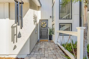 A house with a front porch, a welcome mat, a door with a wreath, and a potted plant. - Luxury NSB Beach House | Private Pool & Bar (New Smyrna Beach)