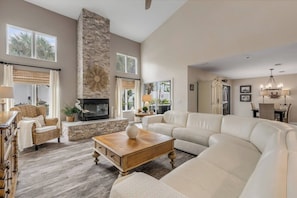 A spacious living room with a fireplace, a sofa, a coffee table, and a dining area with a chandelier. - Luxury NSB Beach House | Private Pool & Bar (New Smyrna Beach)