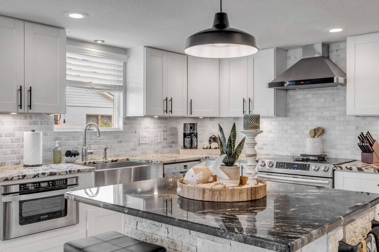 A modern kitchen with white cabinetry, a central island, stainless steel appliances, and a hanging pendant light.