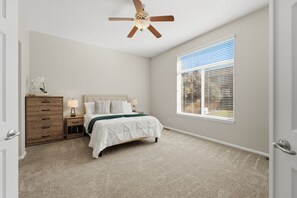 Quarto com cama, mesa de cabeceira, cômoda, ventilador de teto e janela com persianas.