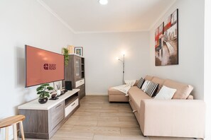 A modern living room with a flat-screen TV, a sofa, a coffee table, a cabinet, and a floor lamp. - GuestReady-Charming Funchal Retreat with Balcony (Funchal)