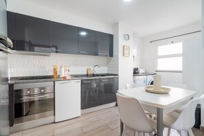 A modern kitchen with stainless steel appliances, a white dining table with chairs, and a window providing natural light. - GuestReady-Charming Funchal Retreat with Balcony (Funchal)