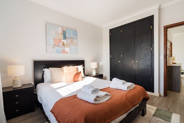A hotel room with a bed, nightstands, a large wardrobe, and a painting on the wall. - GuestReady-Charming Funchal Retreat with Balcony (Funchal)