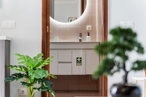 A bathroom with a mirror, sink, and first aid sign. - GuestReady-Charming Funchal Retreat with Balcony (Funchal)