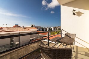 A balcony with wicker furniture, a view of neighboring buildings, and a clear sky. - GuestReady-Charming Funchal Retreat with Balcony (Funchal)