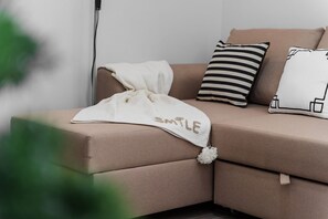 A corner sofa with a white throw blanket and pillows, including a striped one and a geometric-patterned one. - GuestReady-Charming Funchal Retreat with Balcony (Funchal)