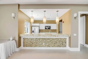 Eine moderne Küche mit weißen Schränken, einer Granitarbeitsplatte und einer Mosaik-Spritzschutzwand. Drei Pendelleuchten und ein Kühlschrank sind vorhanden.