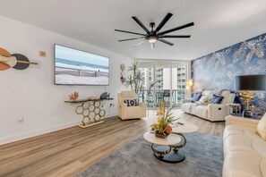 Ein modernes Wohnzimmer mit Deckenventilator, großem Fernseher und Meerblick durch die Balkontüren.