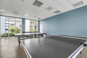 Mesa de pingue-pongue em um quarto com parede azul e janelas amplas.