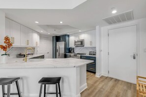A modern kitchen with white cabinetry, a marble island, and a built-in microwave. - 20th Floor Luxury Condo | Halifax River Views (Holly Hill)