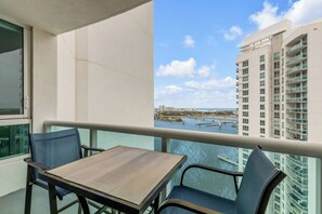 Varanda com mesa e cadeiras, vista para uma marina com barcos e edifícios.