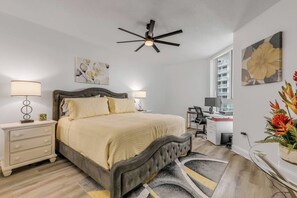 Quarto com cama, mesas de cabeceira, escrivaninha, cadeira, ventilador de teto e obras de arte nas paredes.