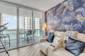 Un salon moderne avec un balcon, un canapé avec des coussins et une table avec des chaises.