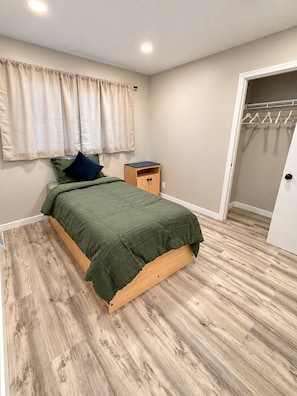 Quarto com cama, mesa de cabeceira, guarda-roupa e janela com cortinas.