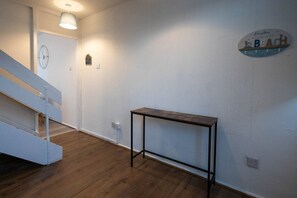 A hallway with a wooden floor, a staircase, a wall-mounted light fixture, and a decorative sign. - 3-bed flat by Felixstowe seafront with roof terrace and parking (Felixstowe)