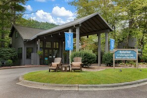 A building with a covered porch, two Adirondack chairs, and a sign indicating Wyndham Resort at Fairfield Sapphire Valley Mountain Laurel Villas Check In. - 1BR Blue Ridge Resort Condo · Indoor Pool, Hot Tub & Tennis · Sapphire NC (Sapphire)