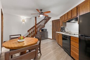 A compact kitchen with wooden cabinets, a black refrigerator, a microwave, and a dining area with a wooden table and chairs. - 1BR Blue Ridge Resort Condo · Indoor Pool, Hot Tub & Tennis · Sapphire NC (Sapphire)