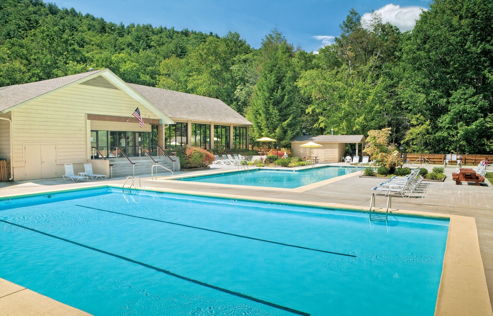 A swimming pool area with lounge chairs and a building with an American flag.