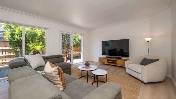 Una sala de estar moderna con un sofá, un sillón, una mesa de centro y un televisor de pantalla plana.