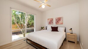 Un dormitorio con cama, mesita de noche, ventilador de techo y dos obras de arte en la pared.