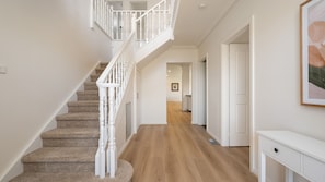 Eine Treppe mit weißen Balustraden führt zu einer zweiten Etage, ein Korridor mit Holzdielen und ein weißer Konsolentisch.