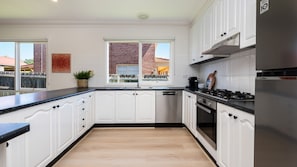 Una cocina con armarios blancos, encimera negra, campana extractora de acero inoxidable y ventana con vistas a un edificio de ladrillo.
