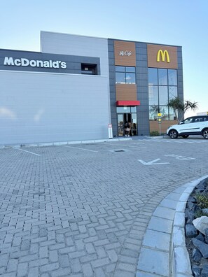 Um restaurante McDonald's com área de entrada pavimentada e um carro branco estacionado por perto.