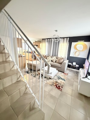 A modern living room with a staircase, a sofa set, a coffee table, and a flat-screen TV. - Luxury Feel, Mountain Views and Comfort at The Town House (Cape Town)