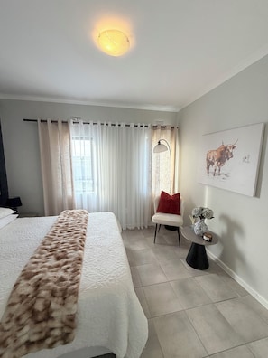 A hotel room with a bed, a chair, a small table with a vase, and a wall-mounted picture. - Luxury Feel, Mountain Views and Comfort at The Town House (Cape Town)