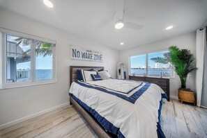 A bedroom with a bed, a 'NO WAKE ZONE' sign, a view of the water, and a large window. - 2-bedroom 2- bath Waterfront Paradise With Intracoastal Views & Dock (West Palm Beach)